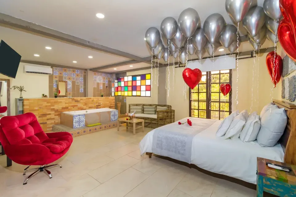 Habitación decorada para planes románticos en Villavicencio, con cama matrimonial, globos en forma de corazón, pétalos, jacuzzi e iluminación cálida.
