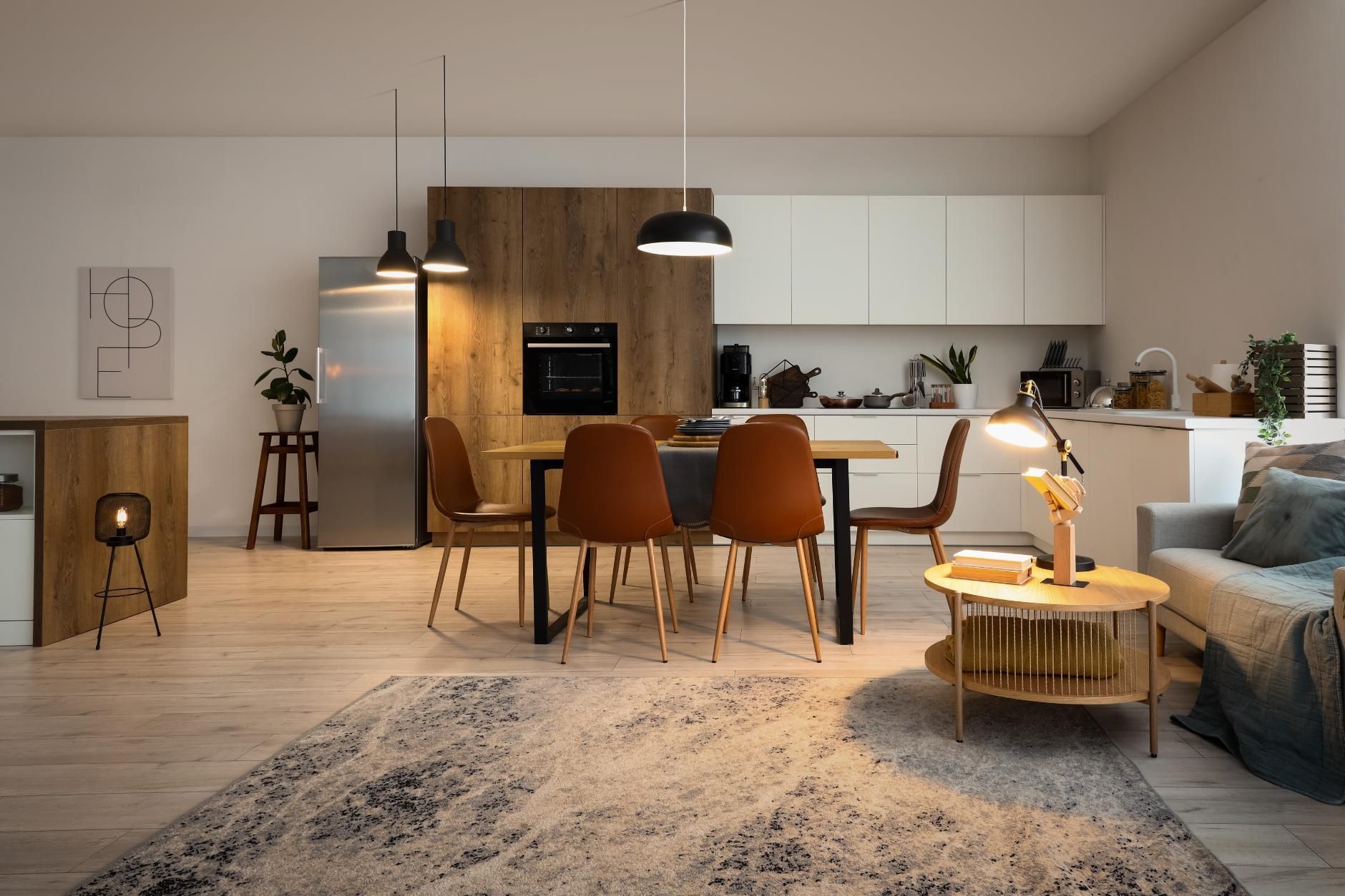Modern open-plan kitchen and living room with wood accents, dining table, sofa, and pendant lights.