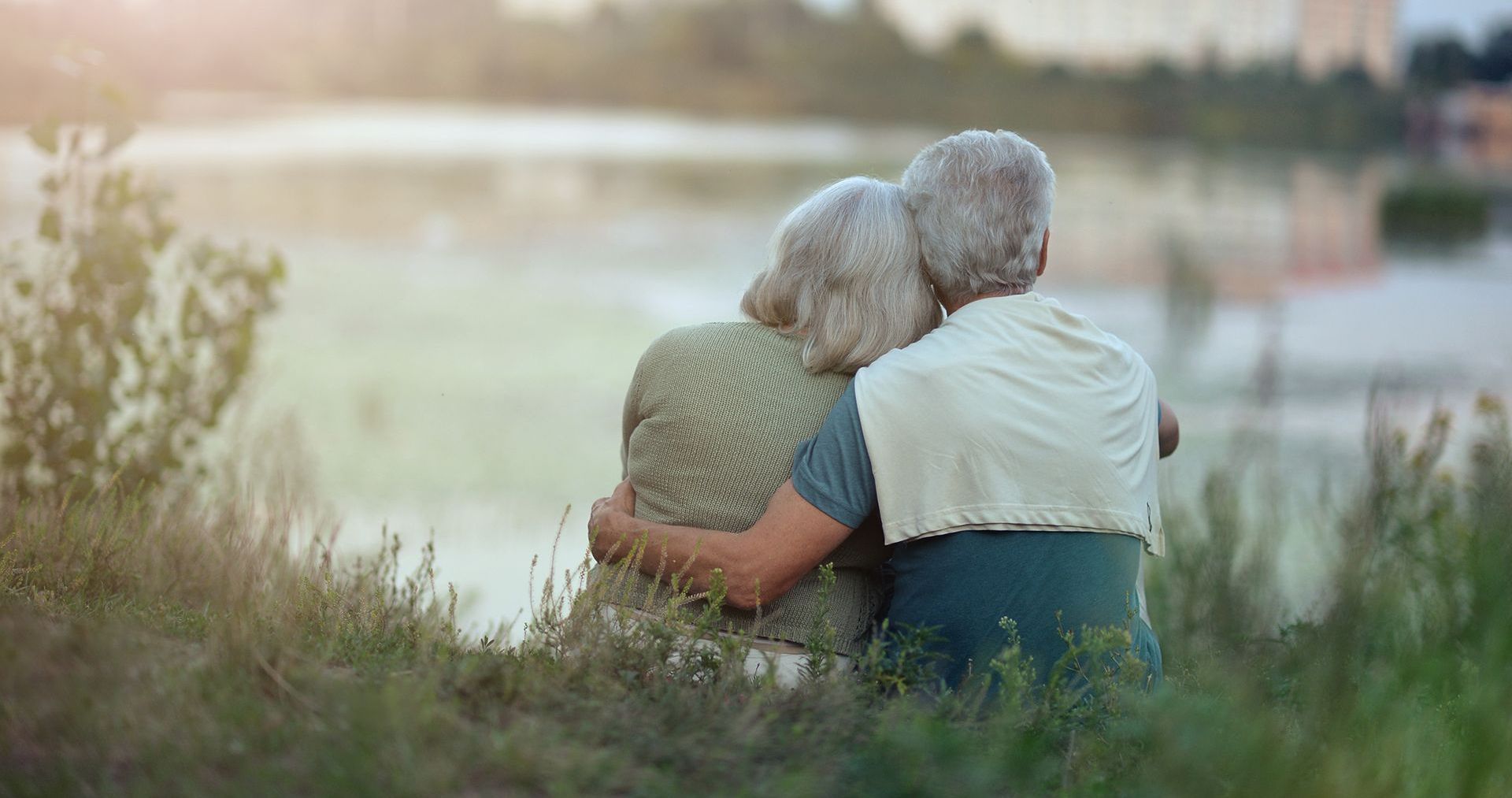An elderly couple is sitting in a field looking at a lake.