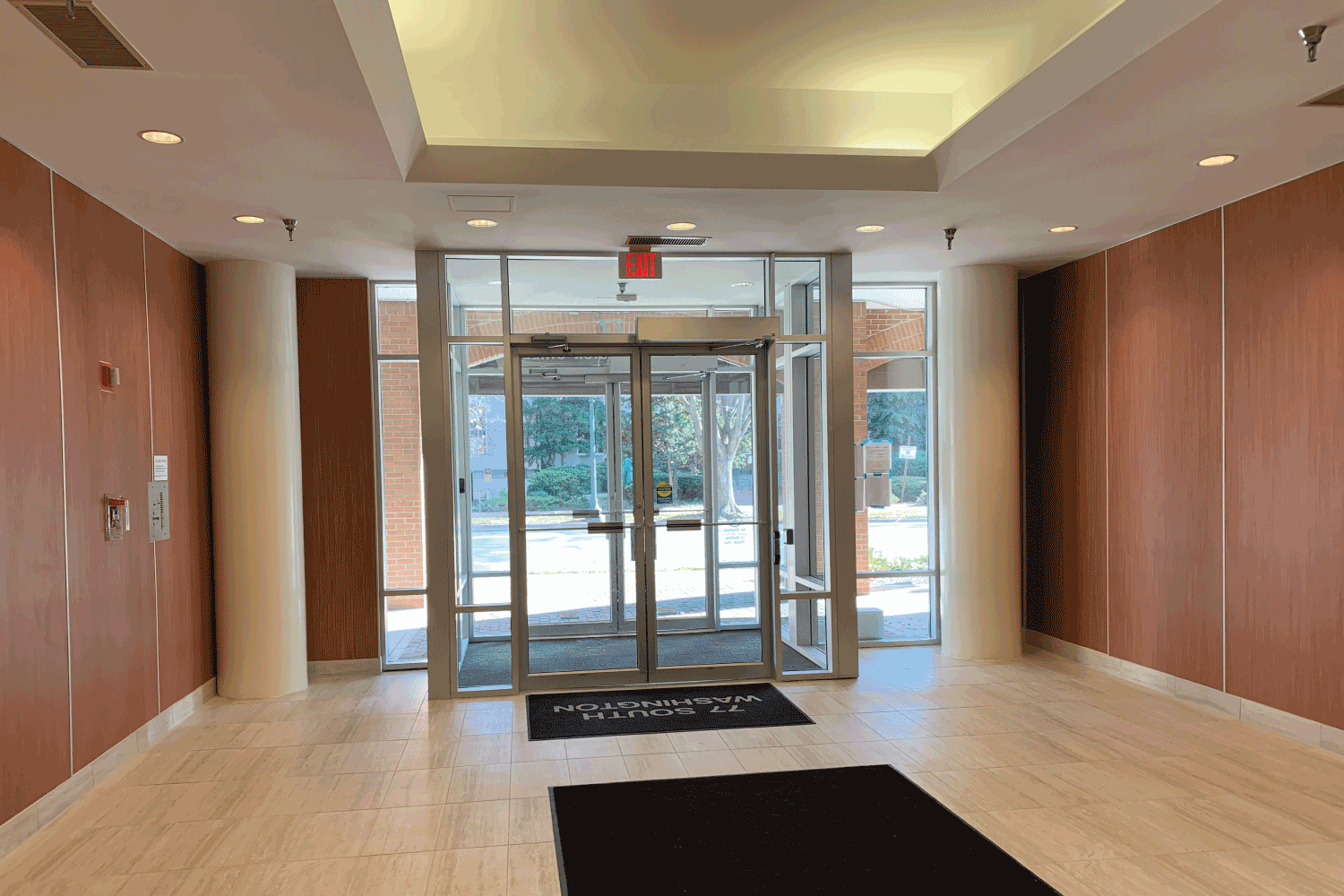 An empty lobby with a sliding glass door and a black mat.