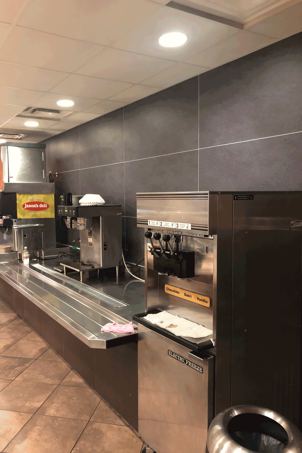A buffet line in a restaurant with a frozen yogurt machine and a trash can.