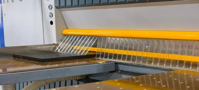 A machine with a yellow bar and protective plastic strips positioned over a flat, dark workpiece on a workspace table.
