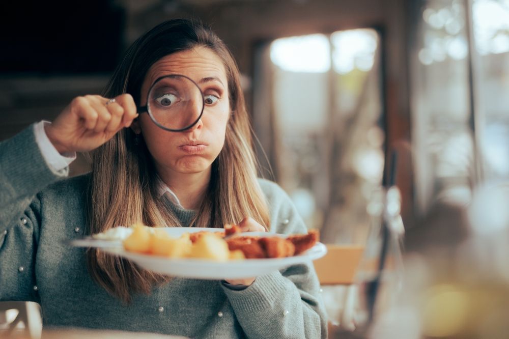 A woman is looking at a plate of food through a magnifying glass.