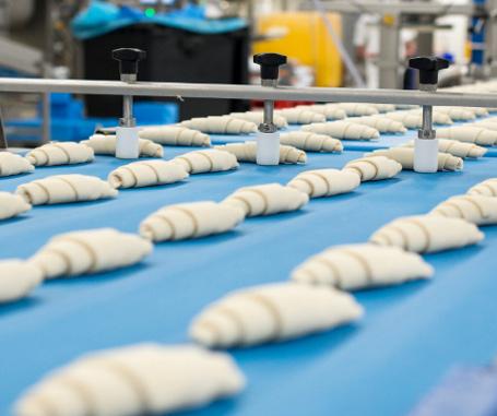 A conveyor belt filled with dough rolls in a bakery