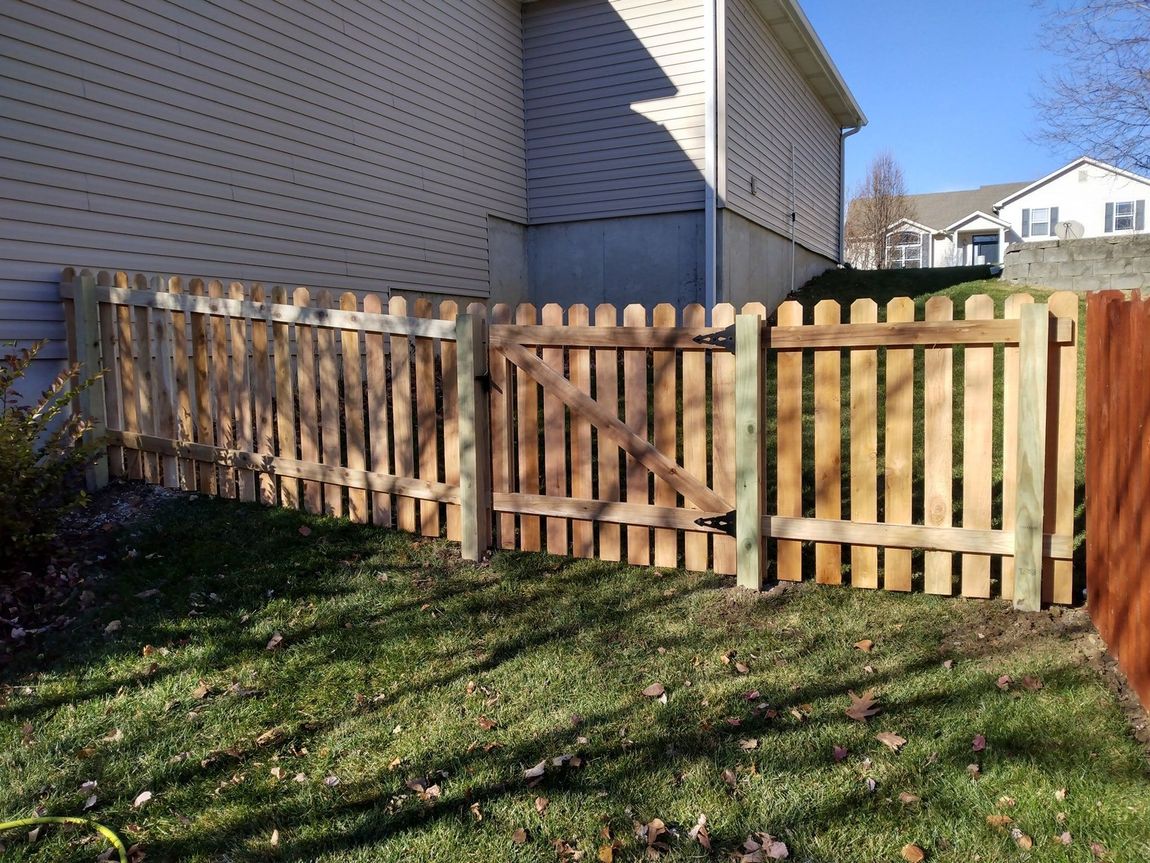 Wooden fence beside a house, with a gate and sunlit grassy yard.