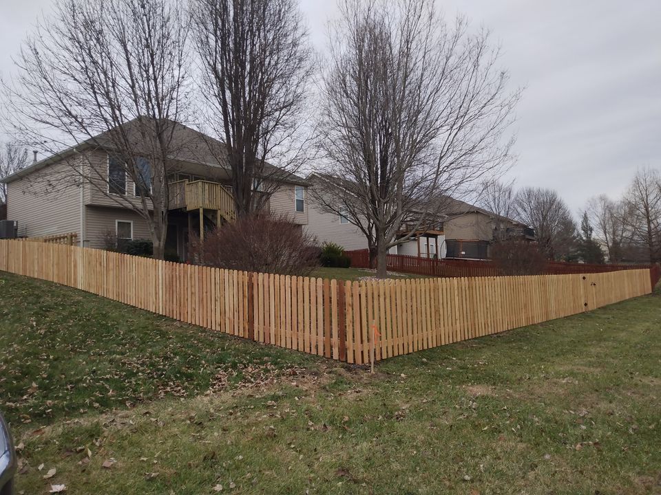 Suburban backyard with a tan house and a long wooden privacy fence under cloudy skies
