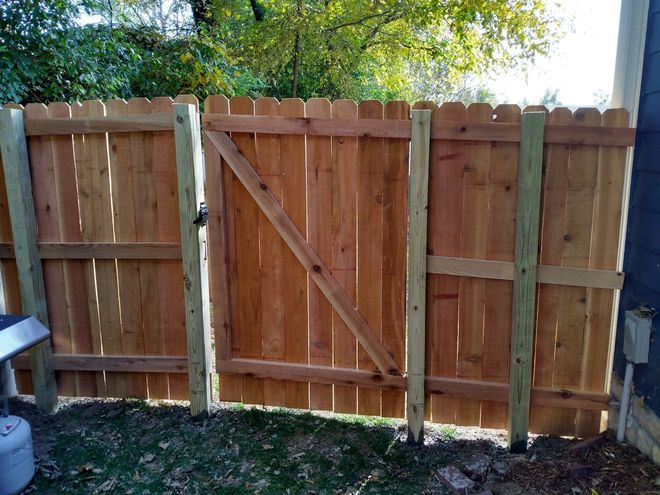 Wooden backyard fence with a central gate and diagonal brace, viewed in daylight