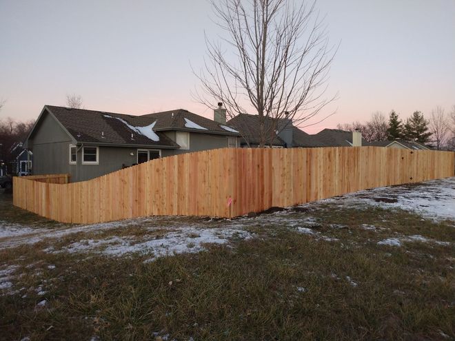 Wooden fence enclosing a gray house and yard at dusk with a pink sky