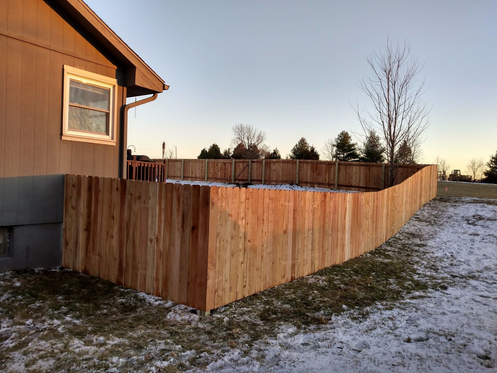 Wooden privacy fence beside a house in a snowy yard at sunset
