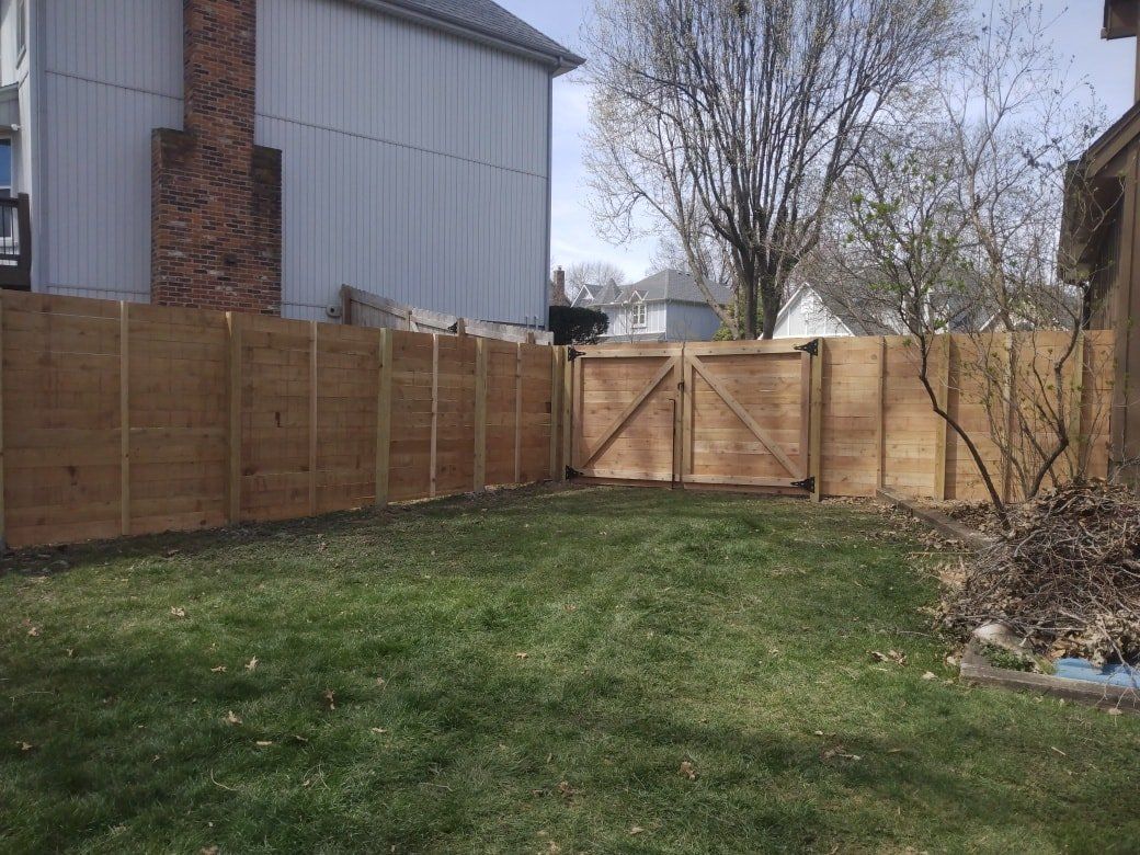 Backyard with grass, wooden fence, and a closed gate beside a house and tree