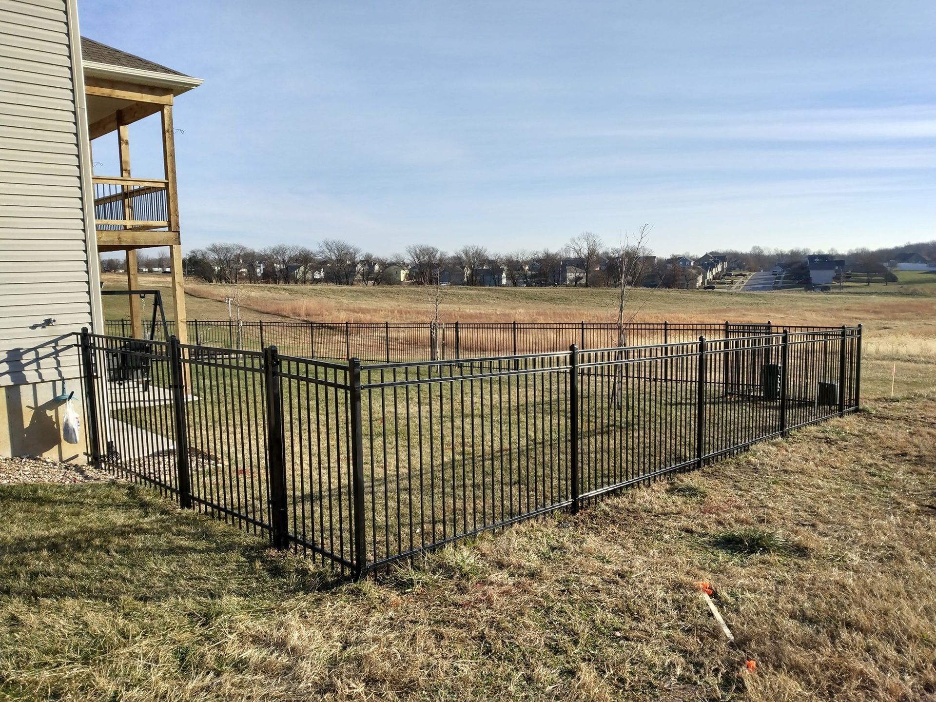 Black metal fence enclosing a grassy yard beside a beige house under a clear sky