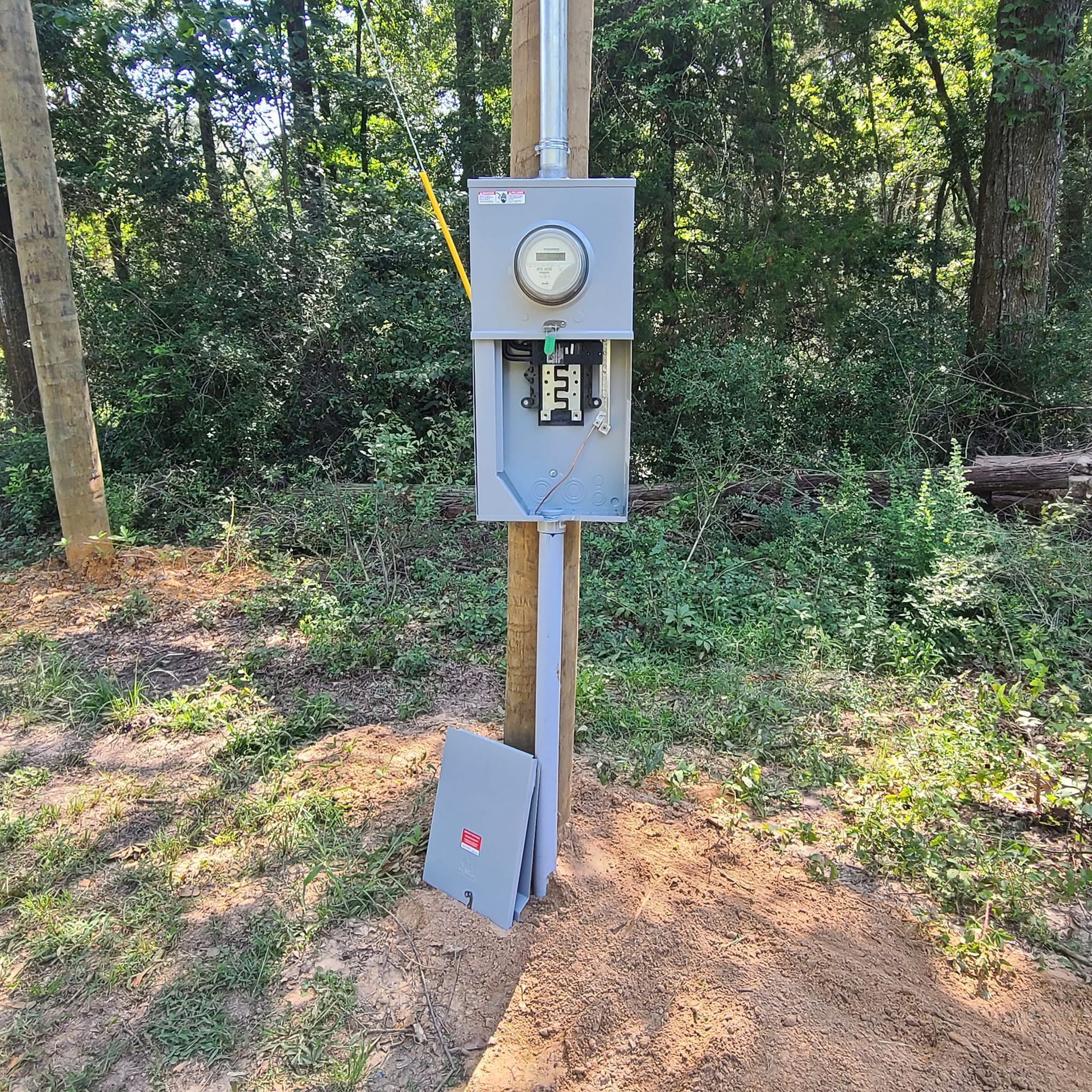 A electrical box is sitting on top of a wooden post in the middle of a field.