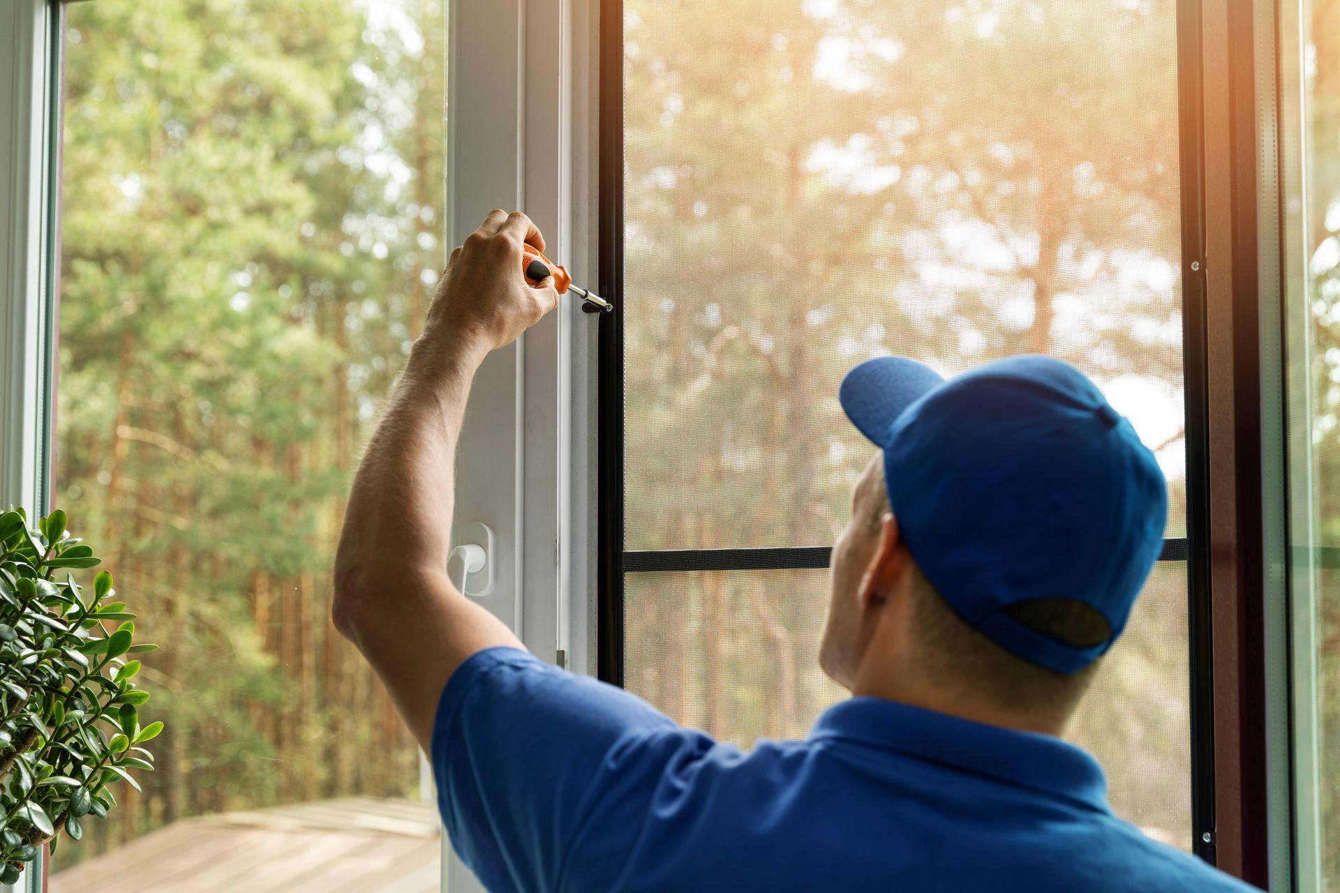 A man installing a mosquito net wire screen on a house window.