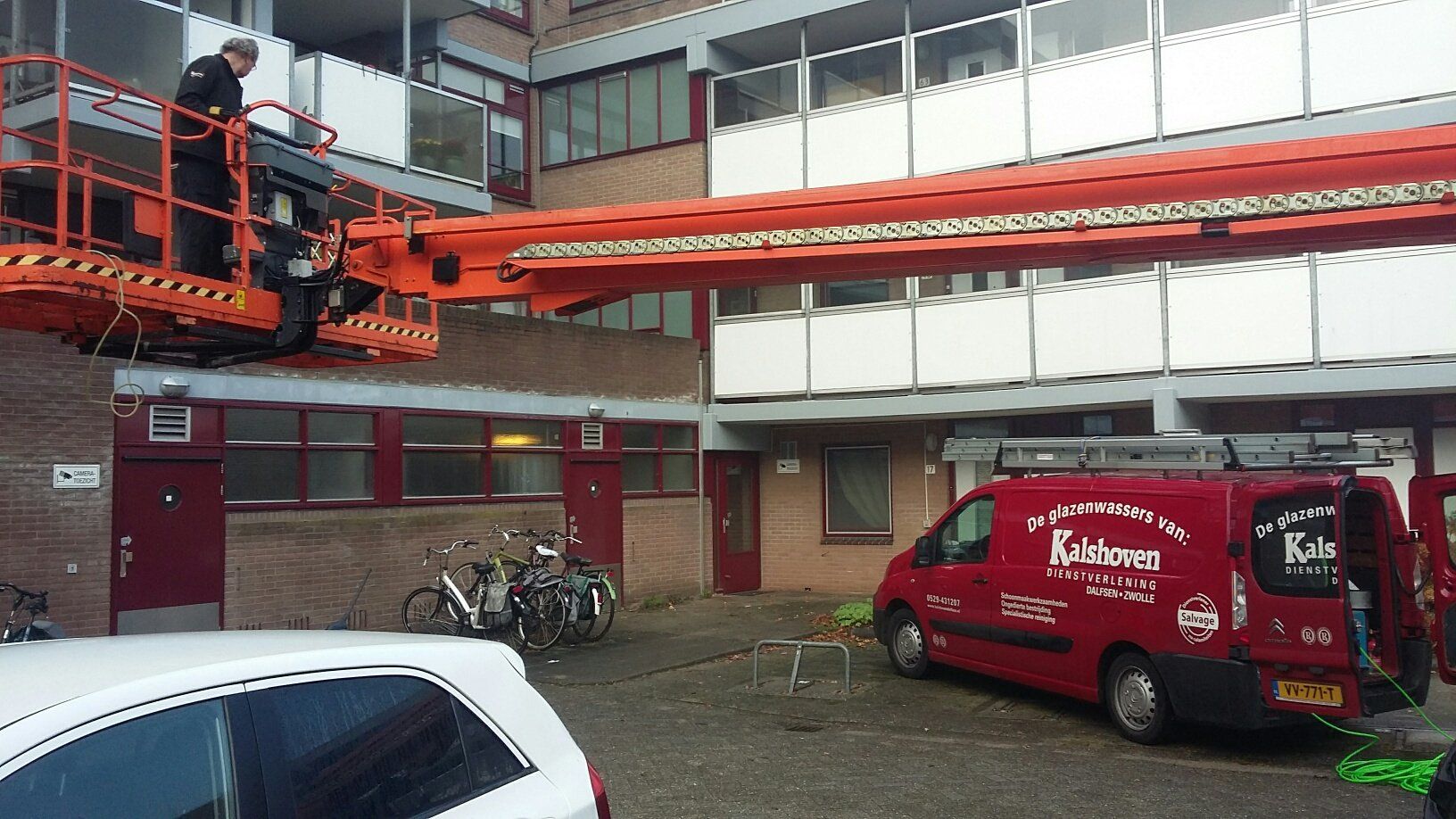 Een rode bestelwagen staat geparkeerd voor een gebouw