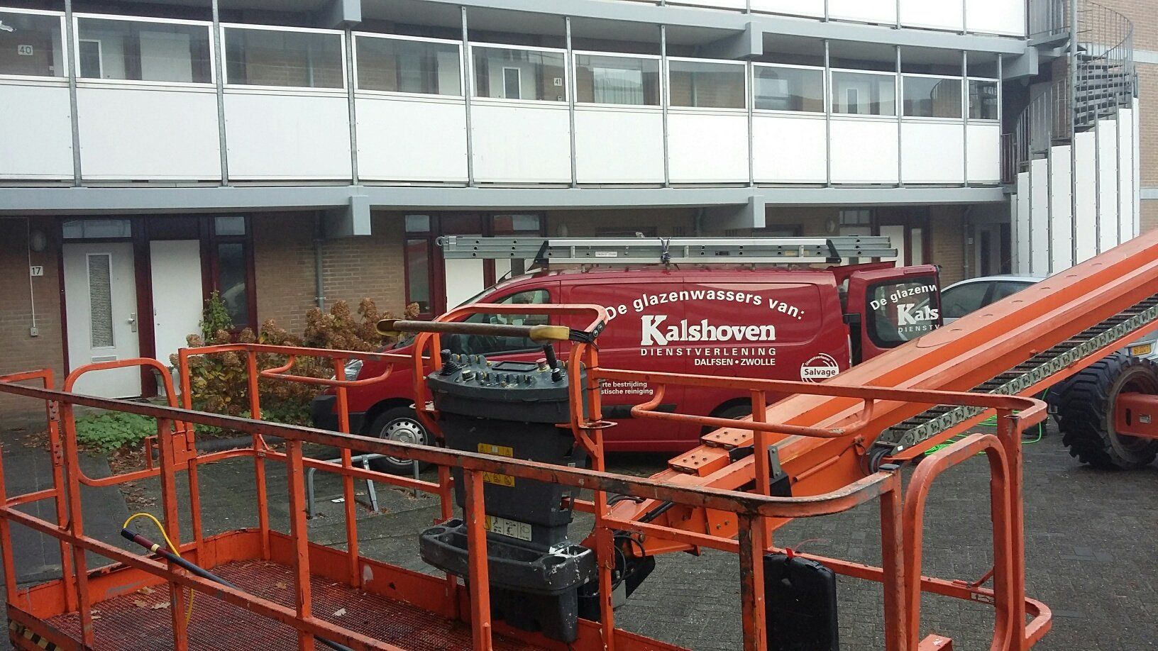 Een rode bestelwagen met het woord kaldschoon erop staat geparkeerd voor een gebouw