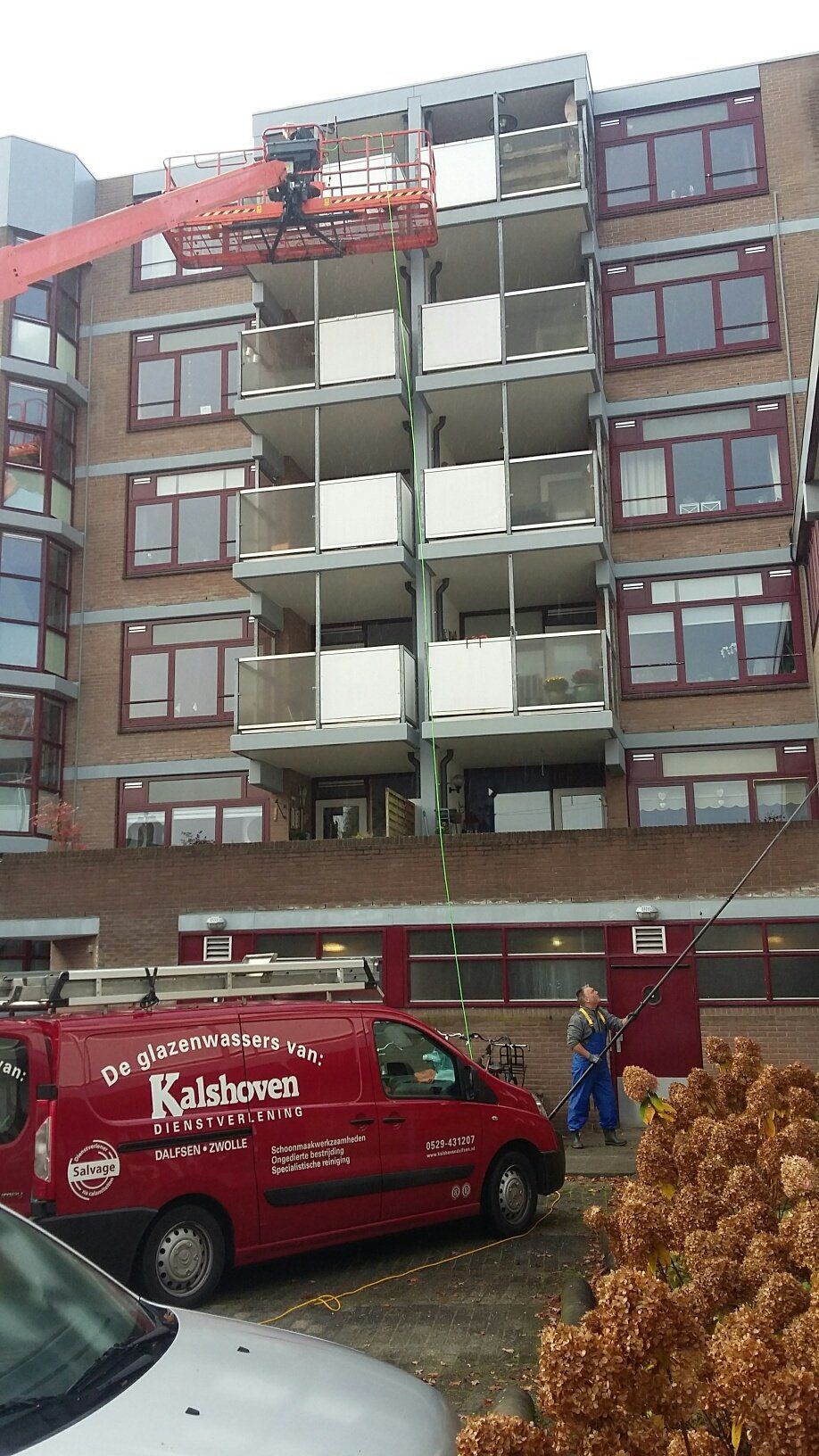 Een rode bestelwagen staat geparkeerd voor een groot gebouw.