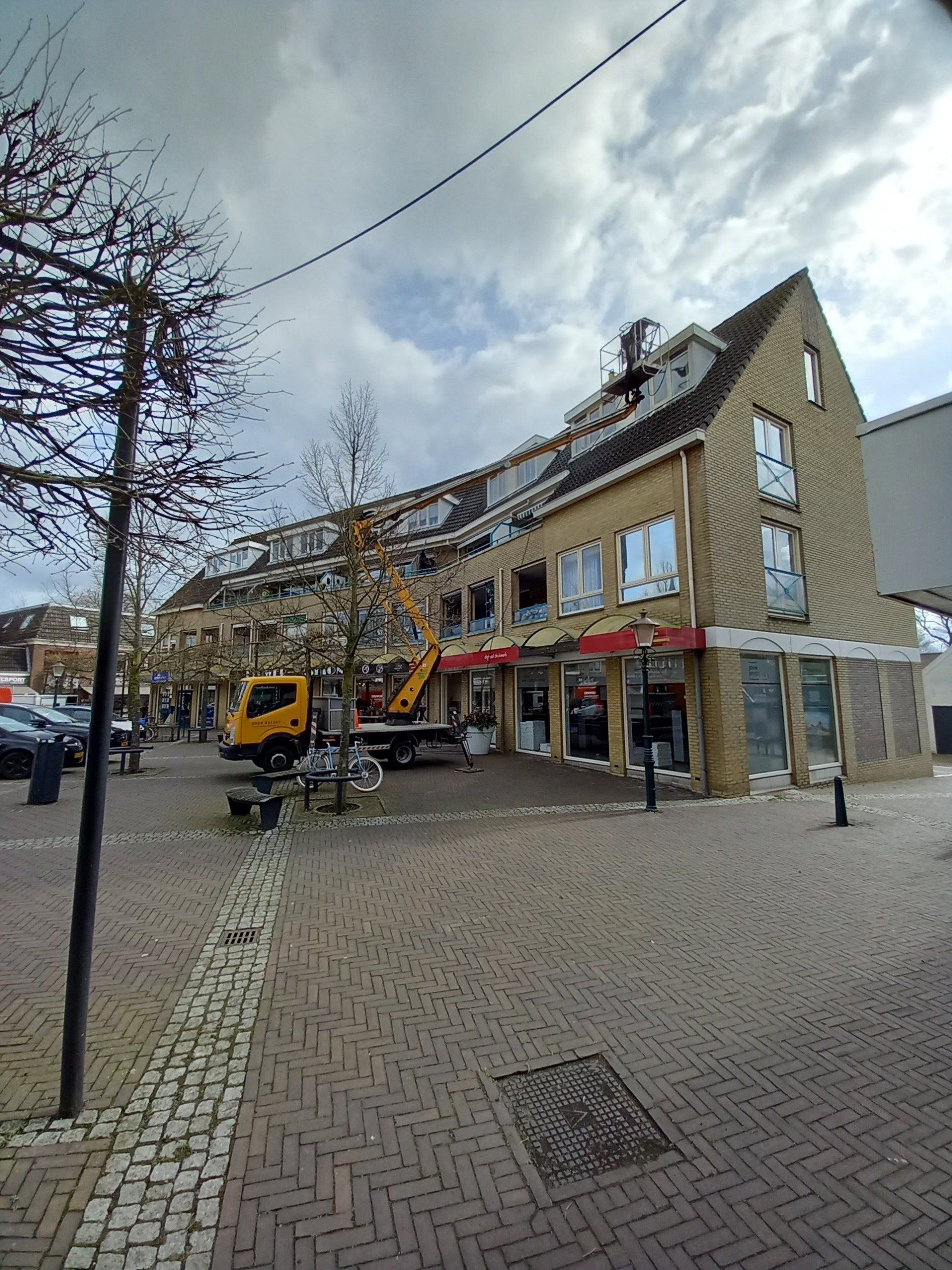Een groot bakstenen gebouw met een gele vrachtwagen ervoor geparkeerd.