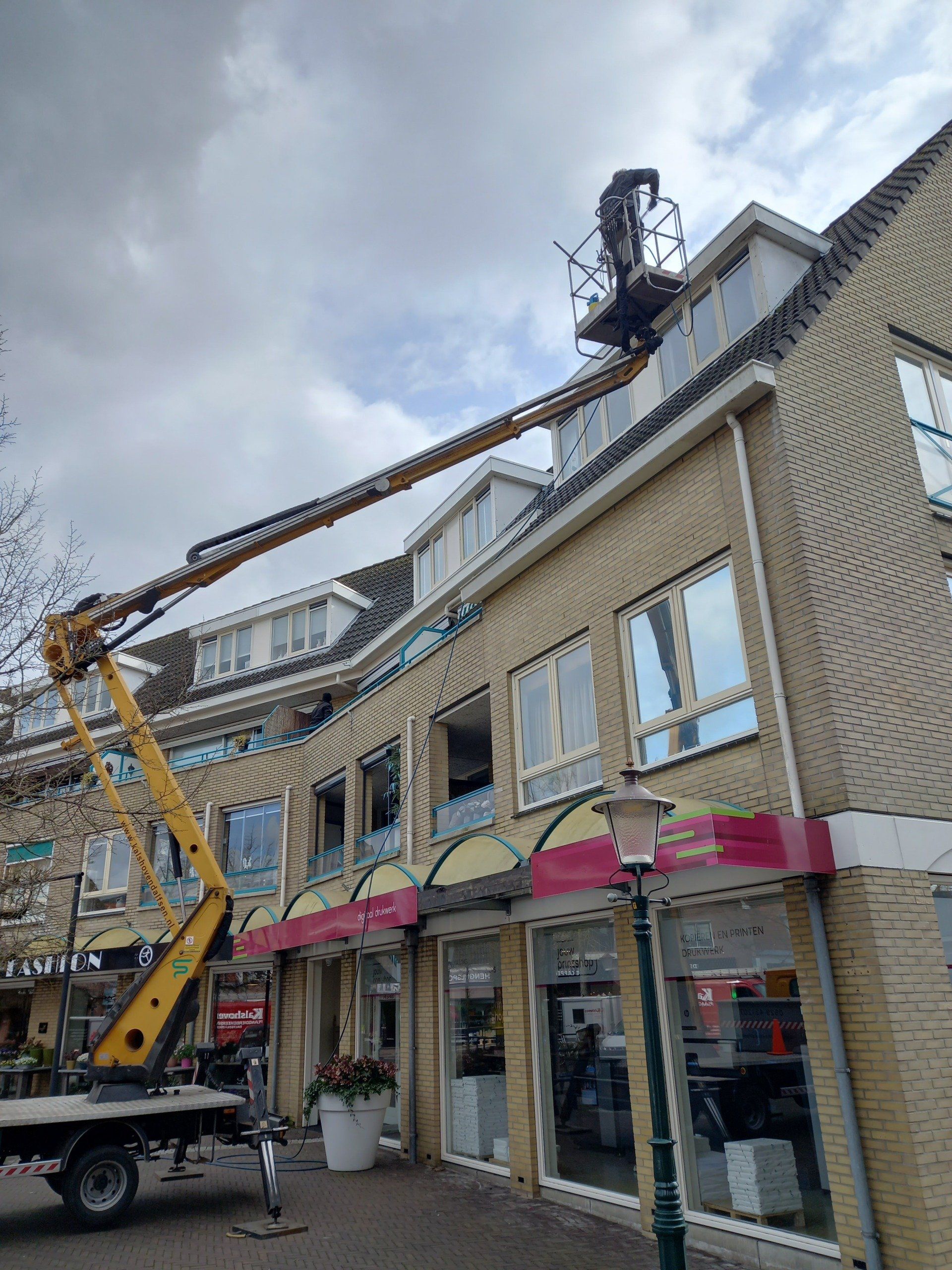 Een man werkt op het dak van een gebouw met een hijskraan.
