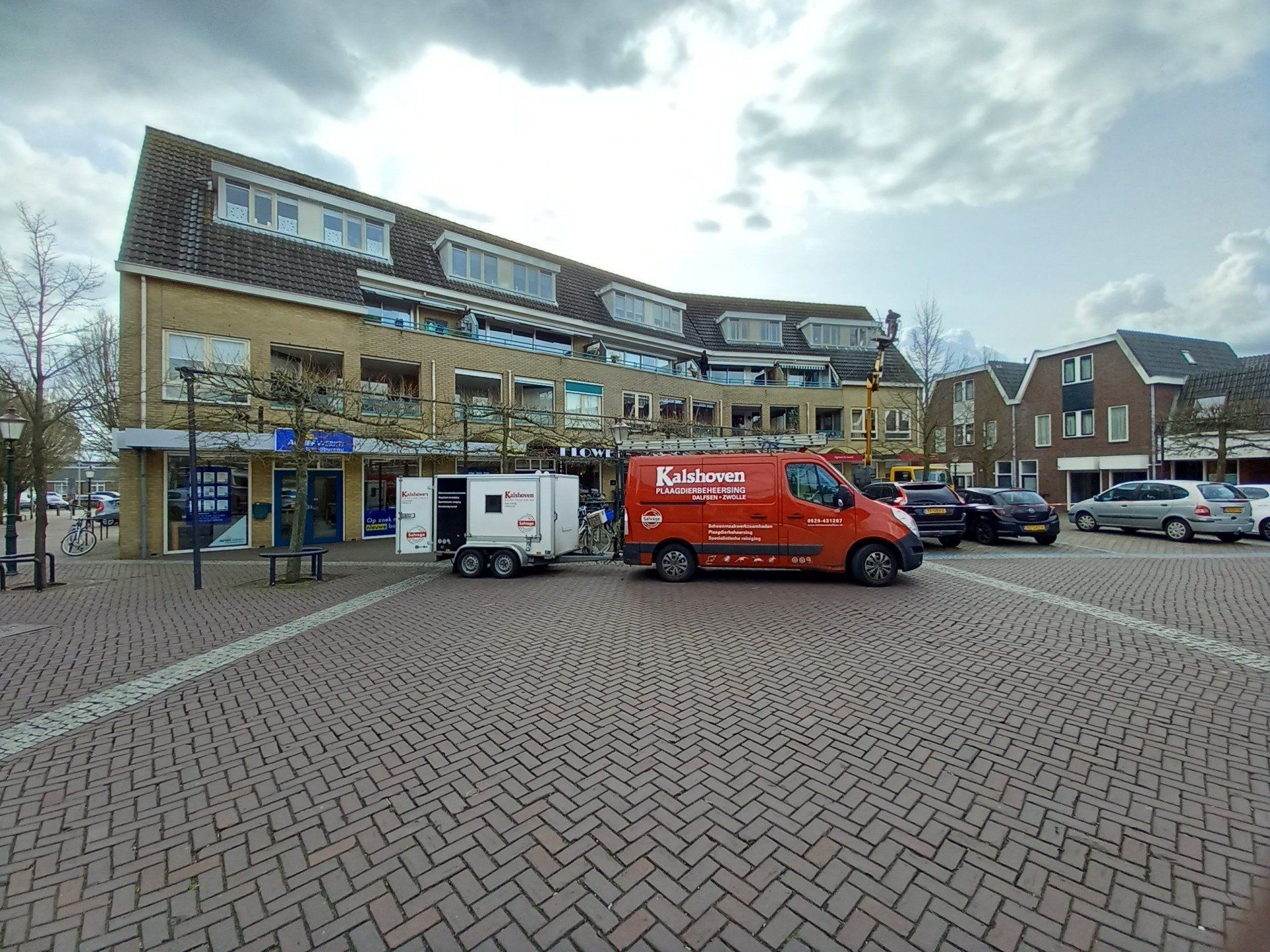 Een rode bestelwagen staat geparkeerd op een parkeerplaats voor een gebouw.