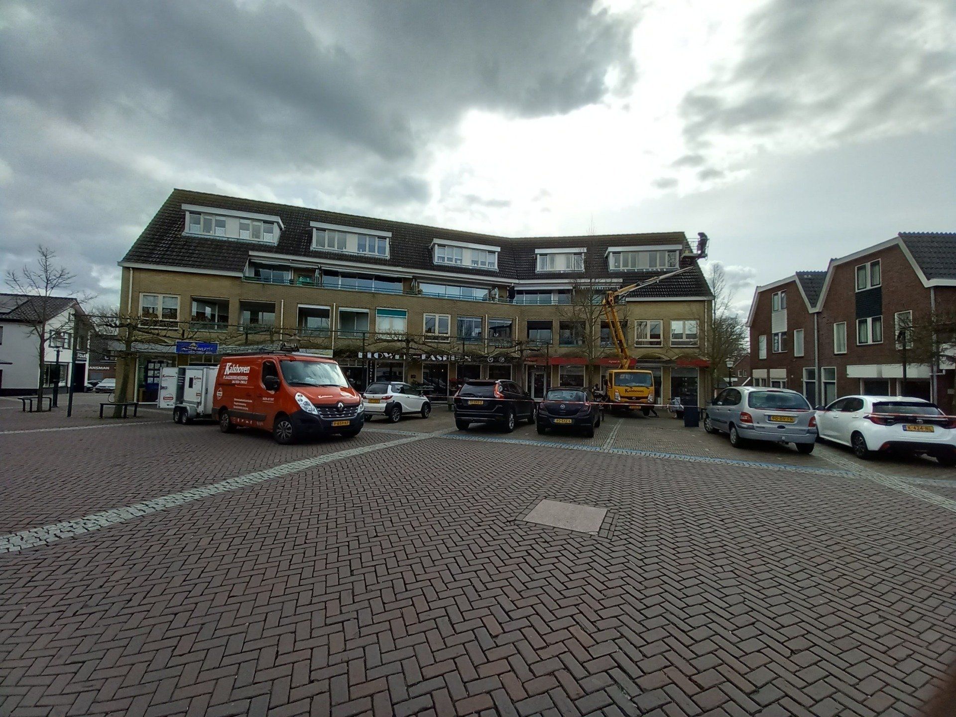Een rode bestelwagen staat geparkeerd op een parkeerplaats voor een gebouw.