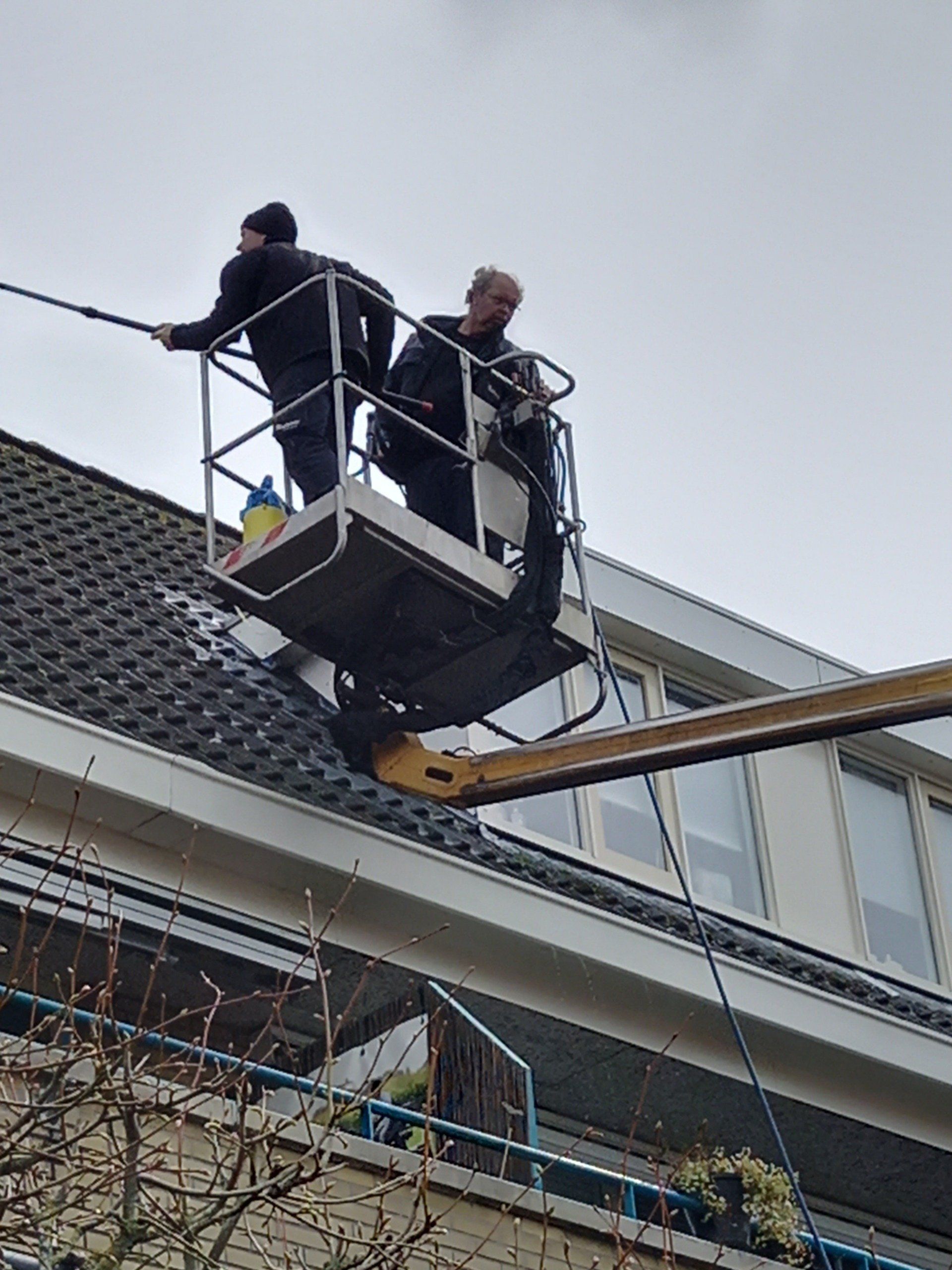 Twee mannen zijn het dak van een gebouw aan het schoonmaken.
