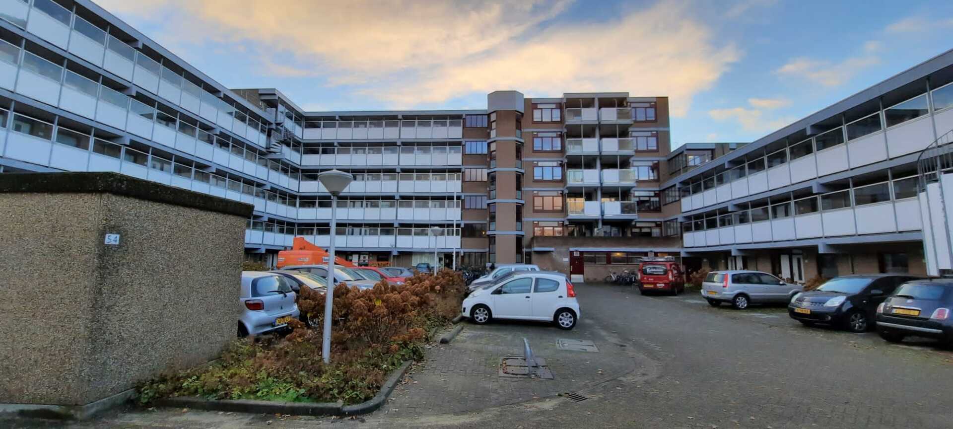 Een parkeerplaats voor een groot appartementengebouw met auto's ervoor geparkeerd.
