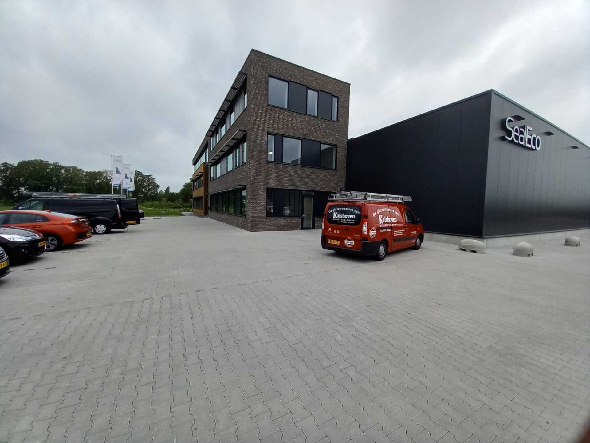 Een rode bestelwagen staat geparkeerd voor een groot gebouw