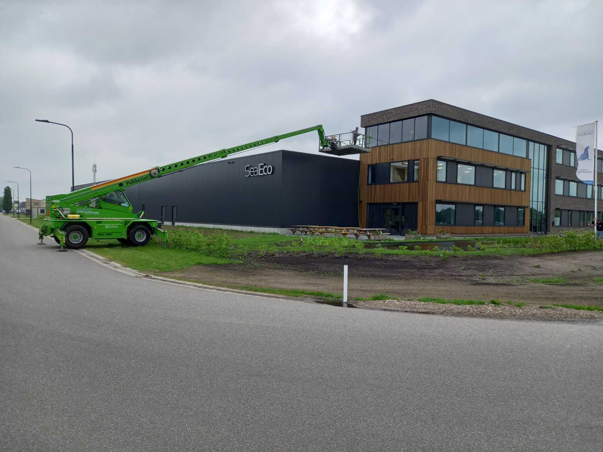 Een groene kraan staat geparkeerd voor een groot gebouw.
