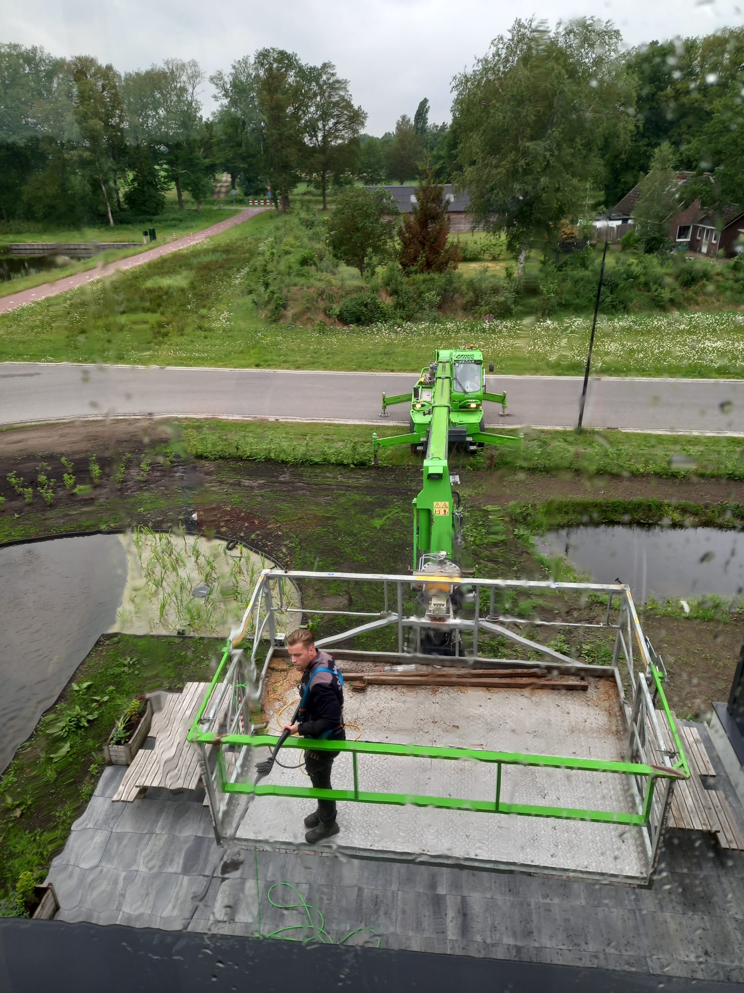 Een man staat op een platform naast een groene kraan.