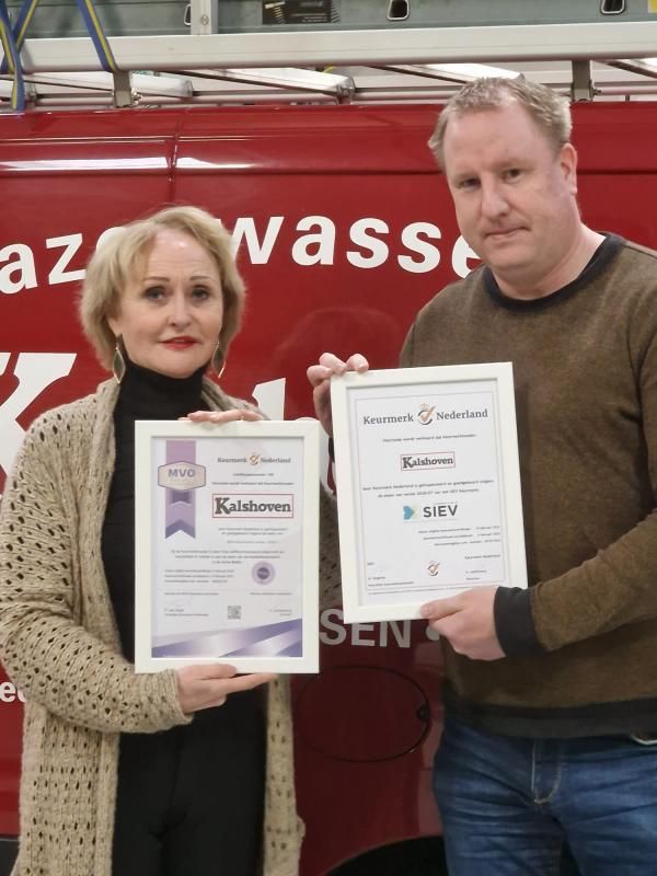 Een man en een vrouw houden certificaten vast voor een rode bestelwagen met het opschrift azwass