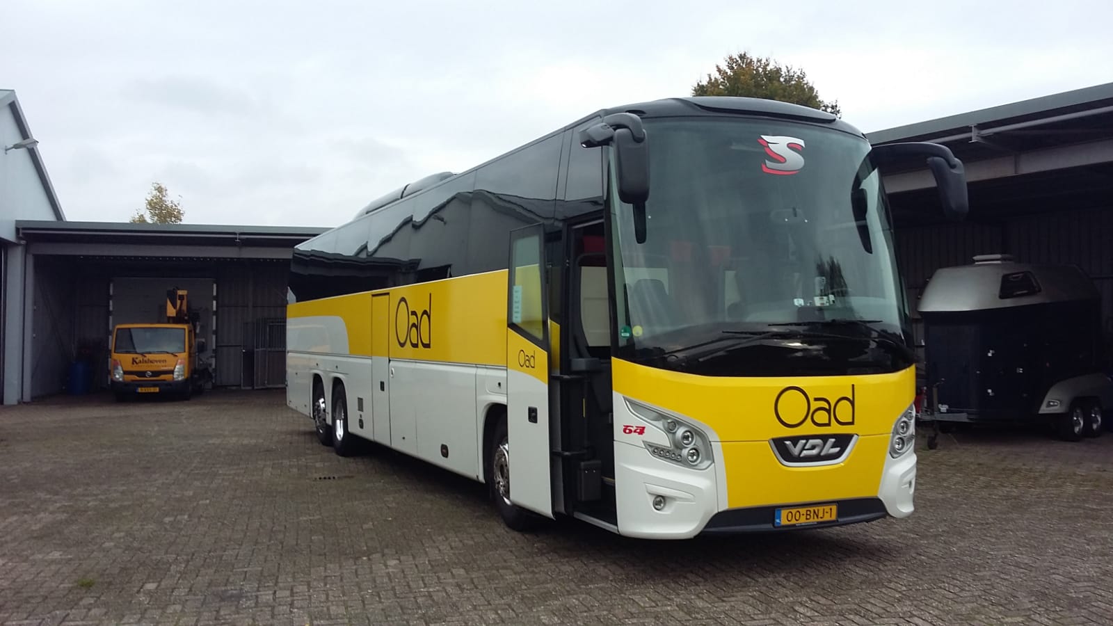 Een geel-witte bus staat geparkeerd voor een gebouw.