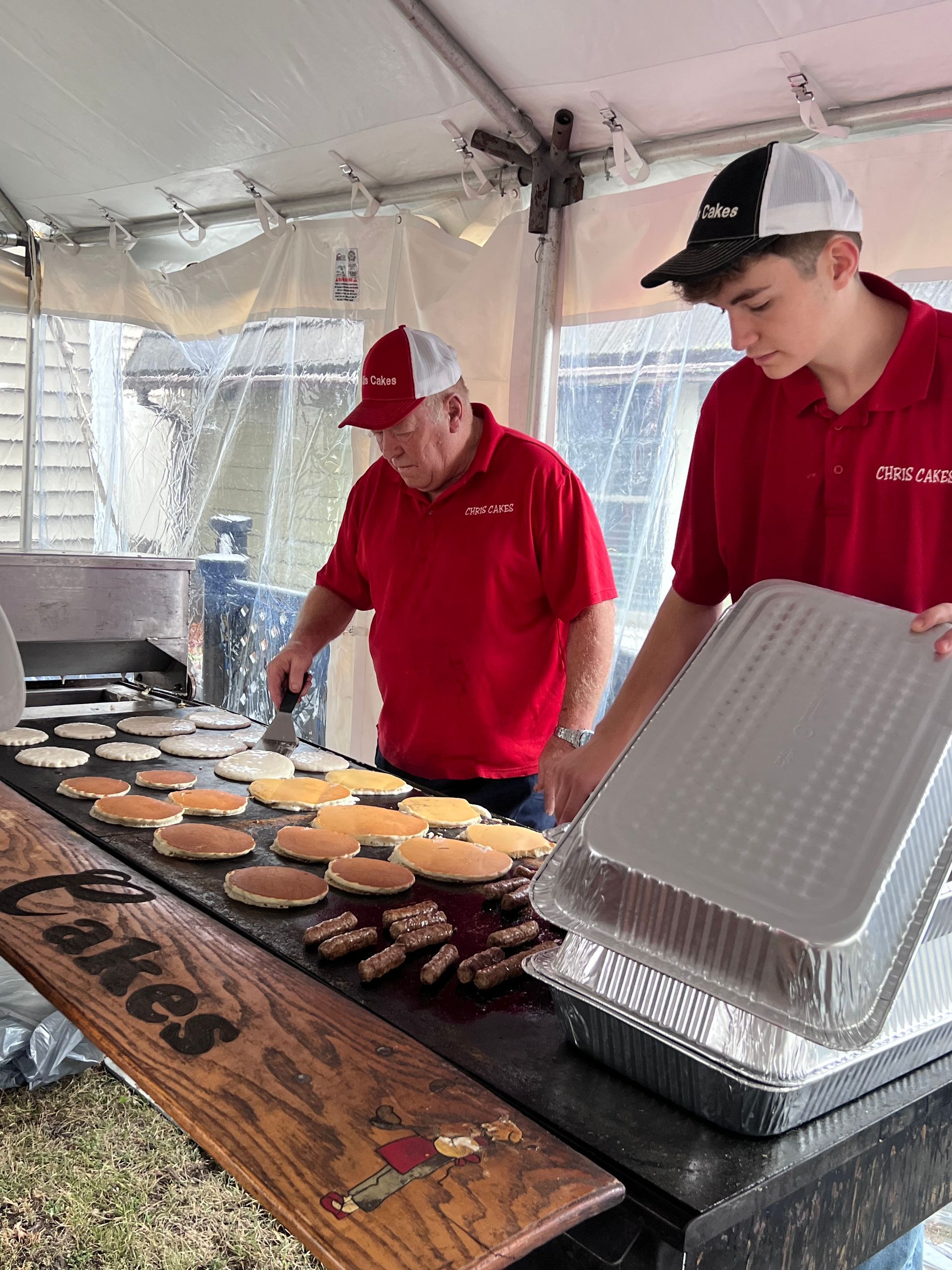 Two men in red shirts are preparing food on a griddle