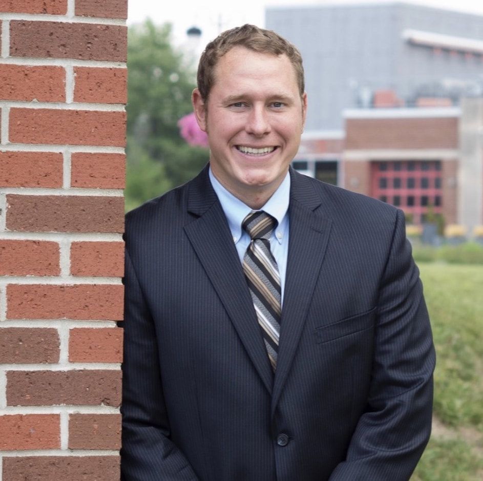 A man in a suit and tie leans against a brick wall