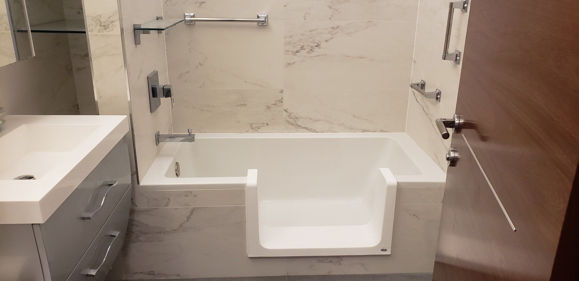 Accessible bathroom with step-in tub, white sink, and wood door