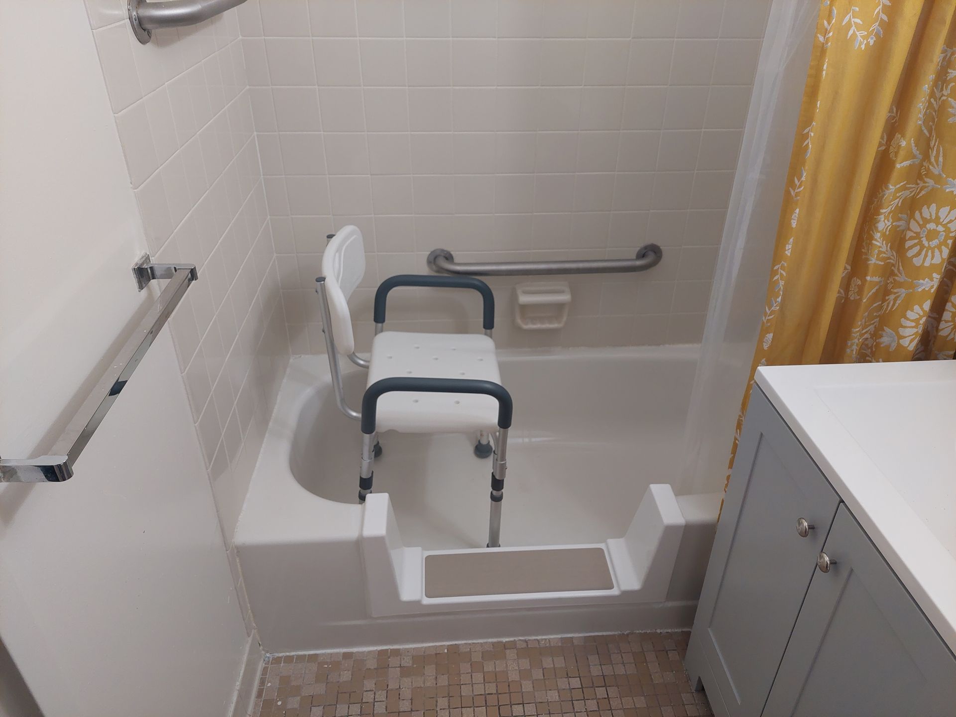 Accessible bathroom with step-in tub bench, grab bars, and curtain beside sink cabinet