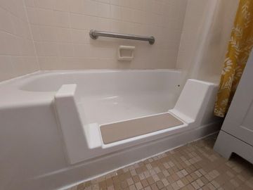 Accessible bathtub with built-in seat and grab bar in a tiled bathroom