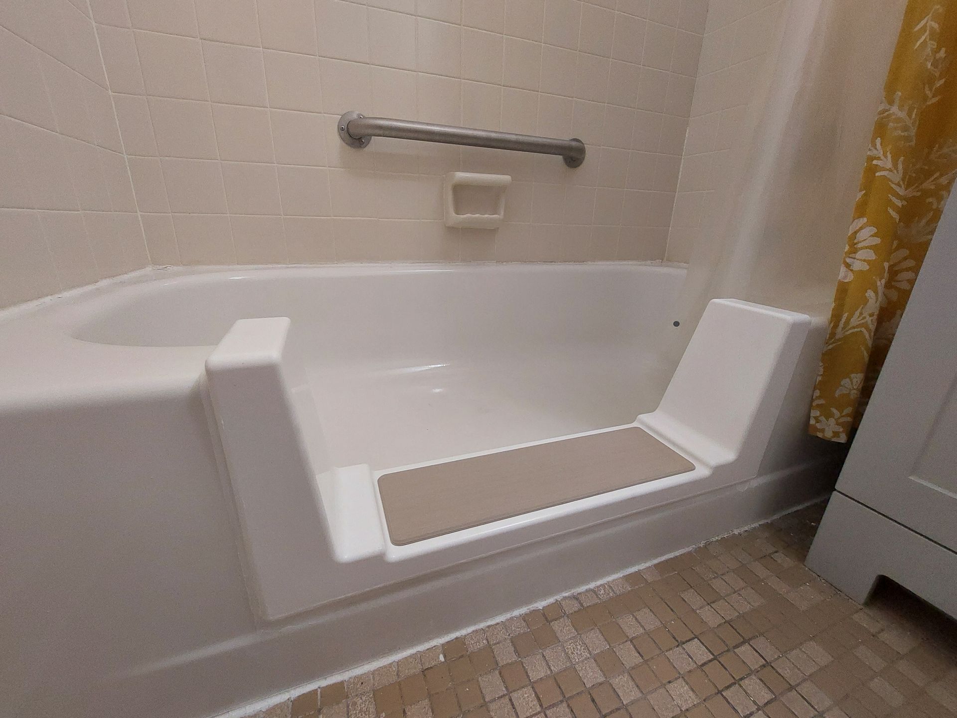 Accessible step-in bathtub with built-in seat, grab bar, and tiled bathroom floor