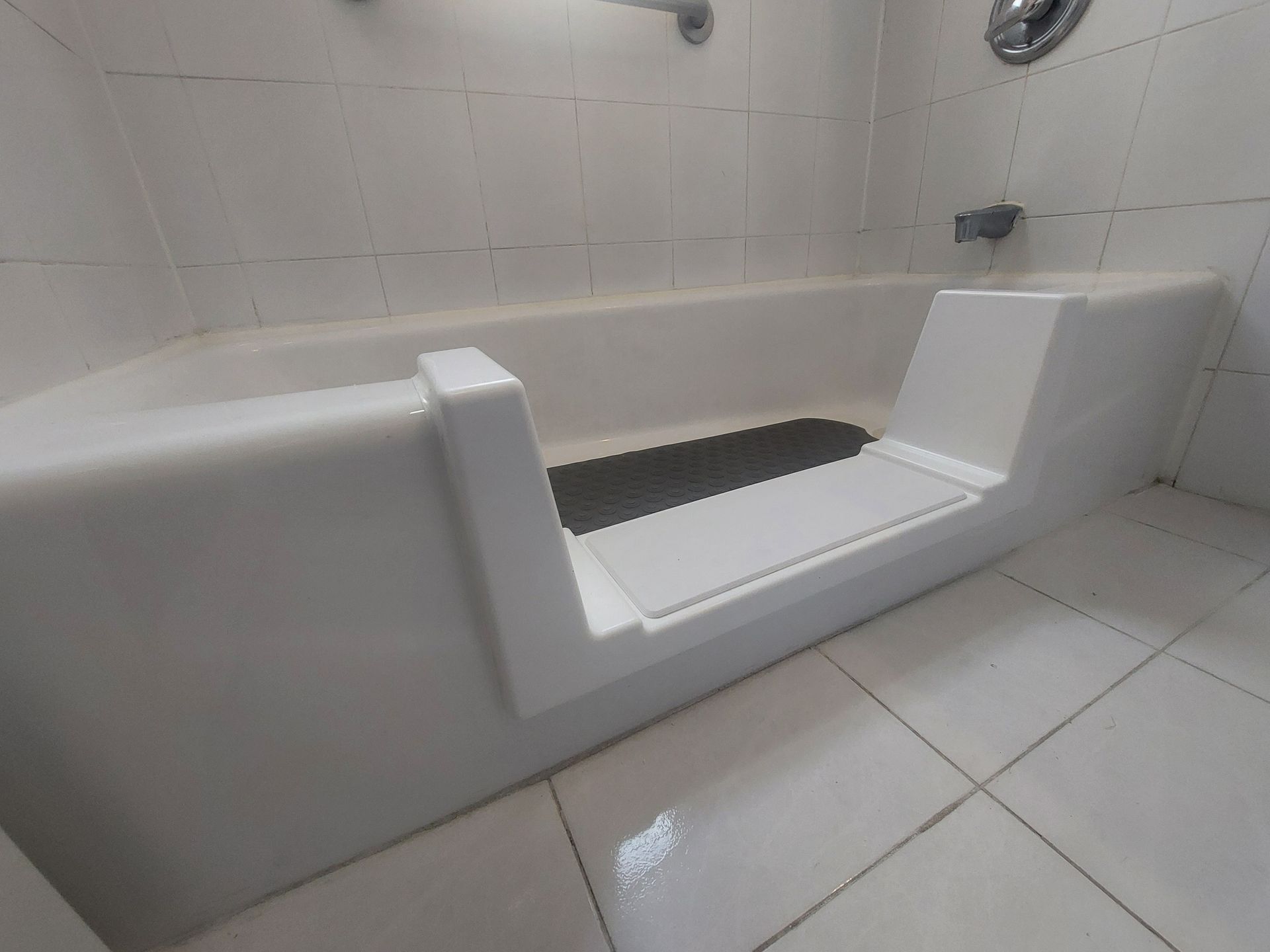 White step-in bathtub with a built-in transfer bench in a tiled bathroom