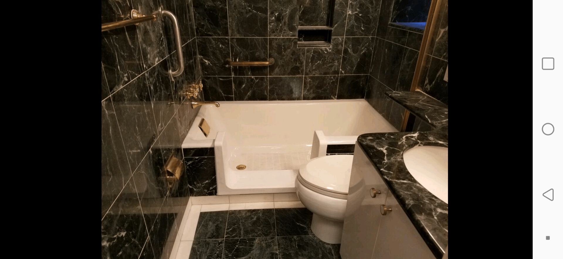 Black marble bathroom with step-in bathtub, toilet, and sink in a compact, glossy tiled space