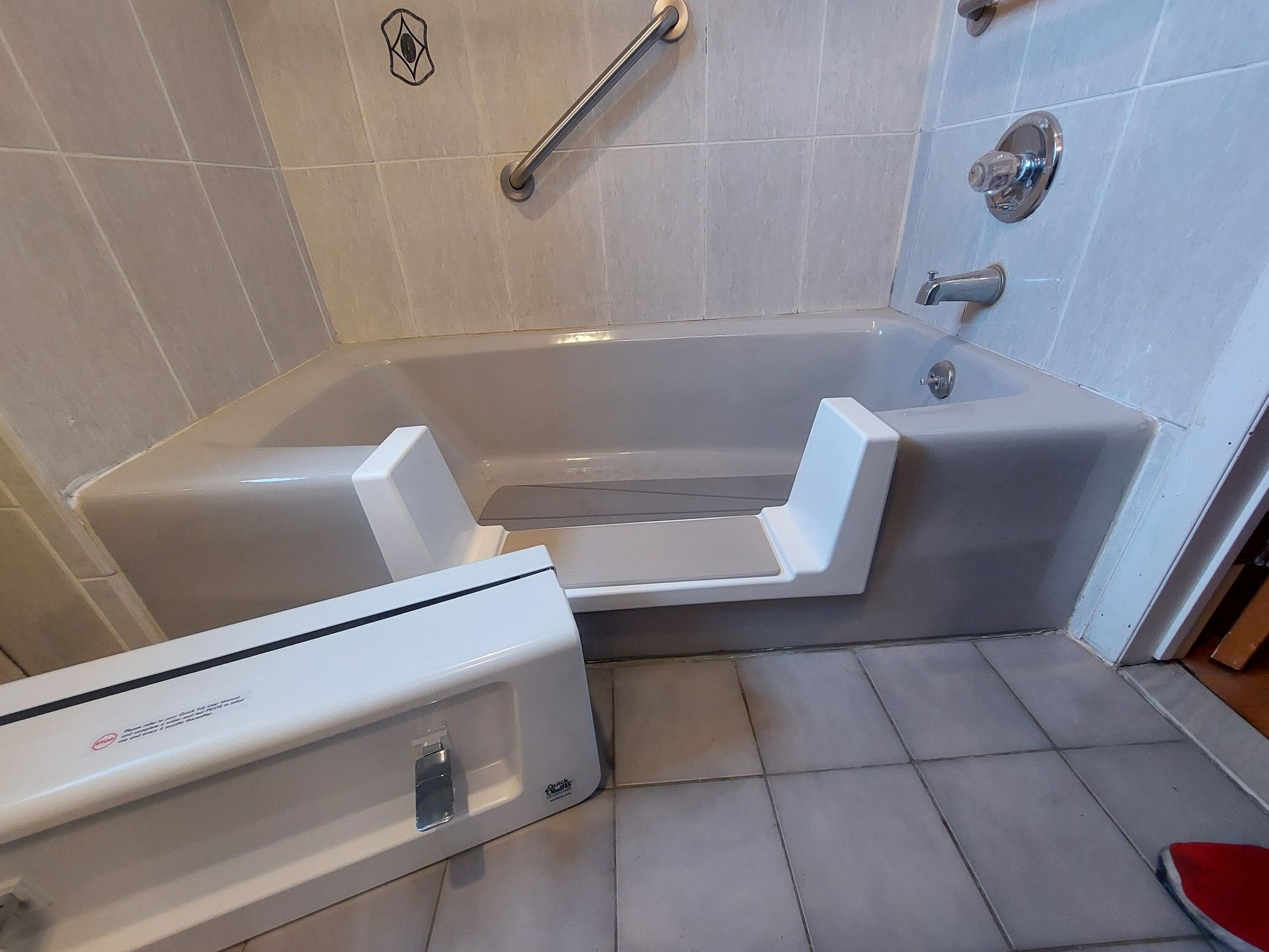 Accessible step-in bathtub with built-in seat, grab bars, and a fold-down safety panel in a tiled bathroom