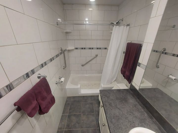 Accessible bathroom with step-in tub, shower curtain, grab bars, and maroon towels