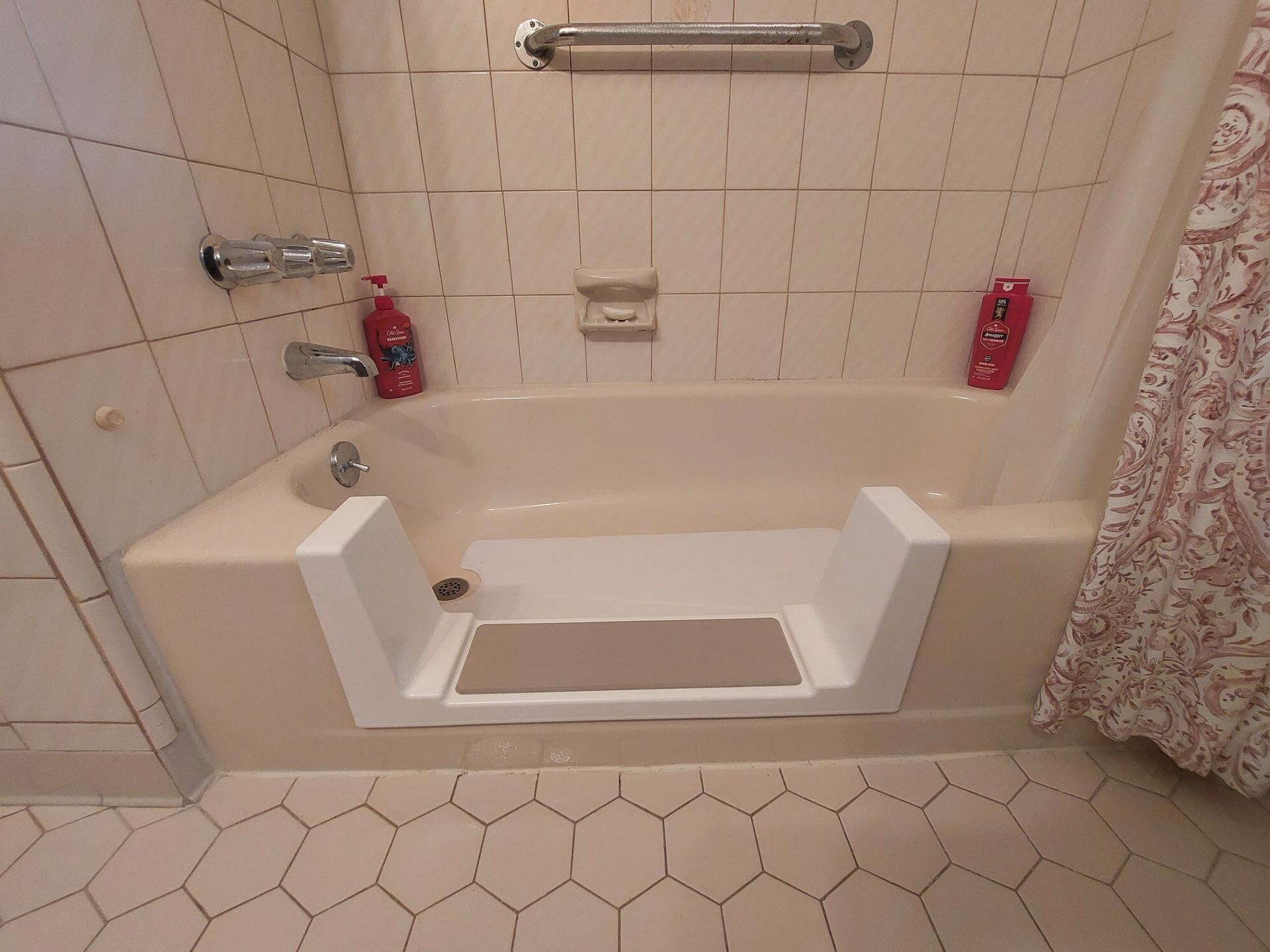 Bathroom with a step-in bathtub, built-in step seat, tiled walls, and hexagonal floor tiles.