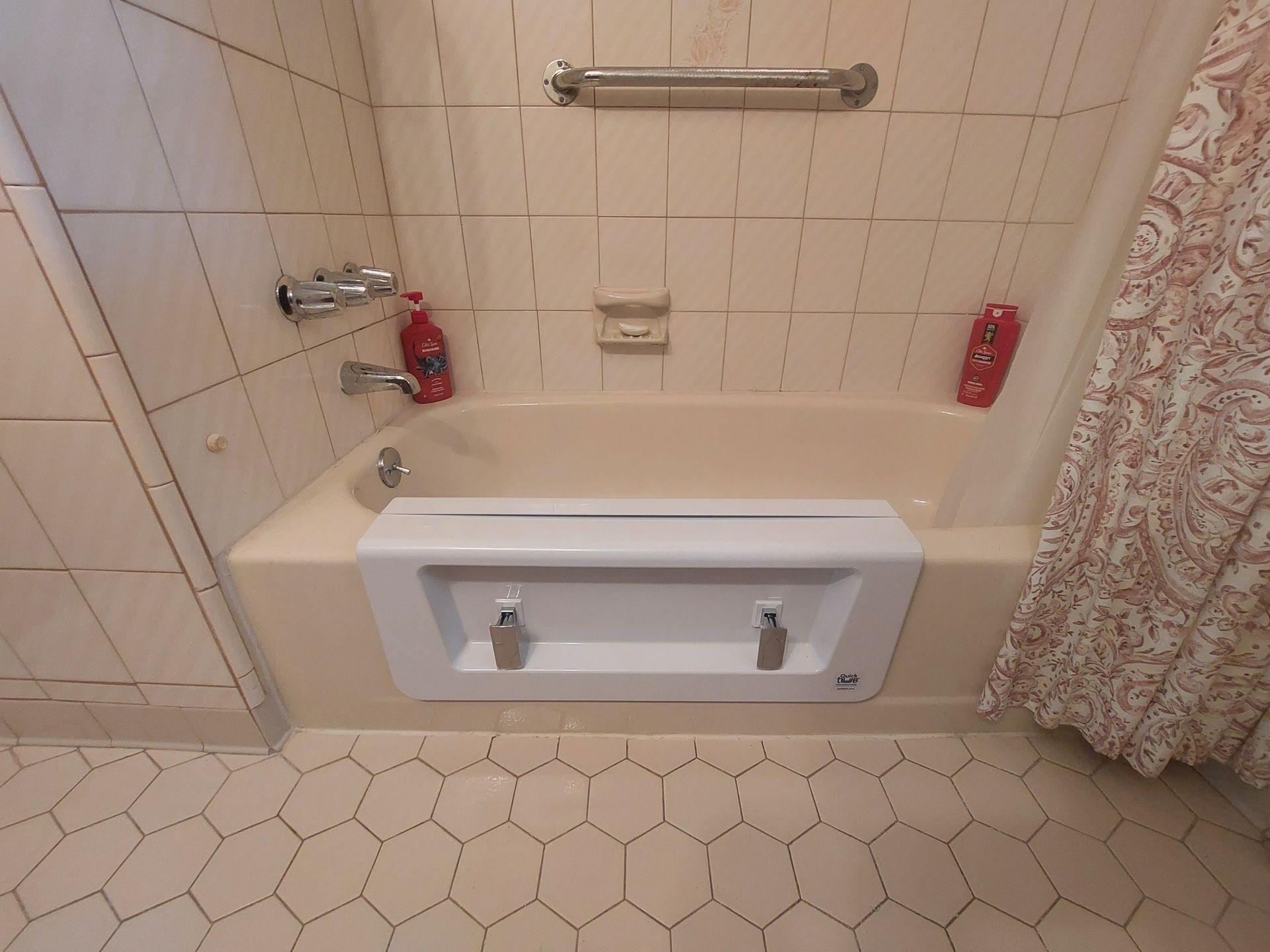 Accessible step-in bathtub with grab bars, shower controls, and tile walls in a small bathroom