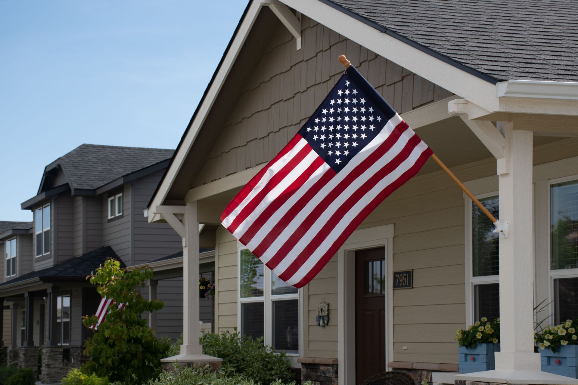 American flag hanging from a suburban house porch with beige siding and white trim
