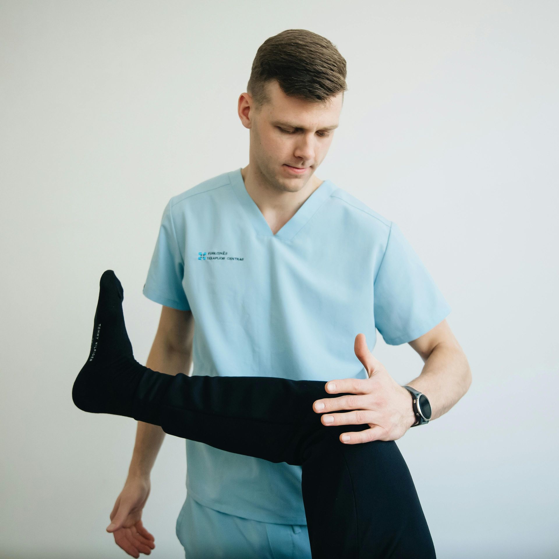 Physical therapist in light blue scrubs stretching a patient's black-clad leg