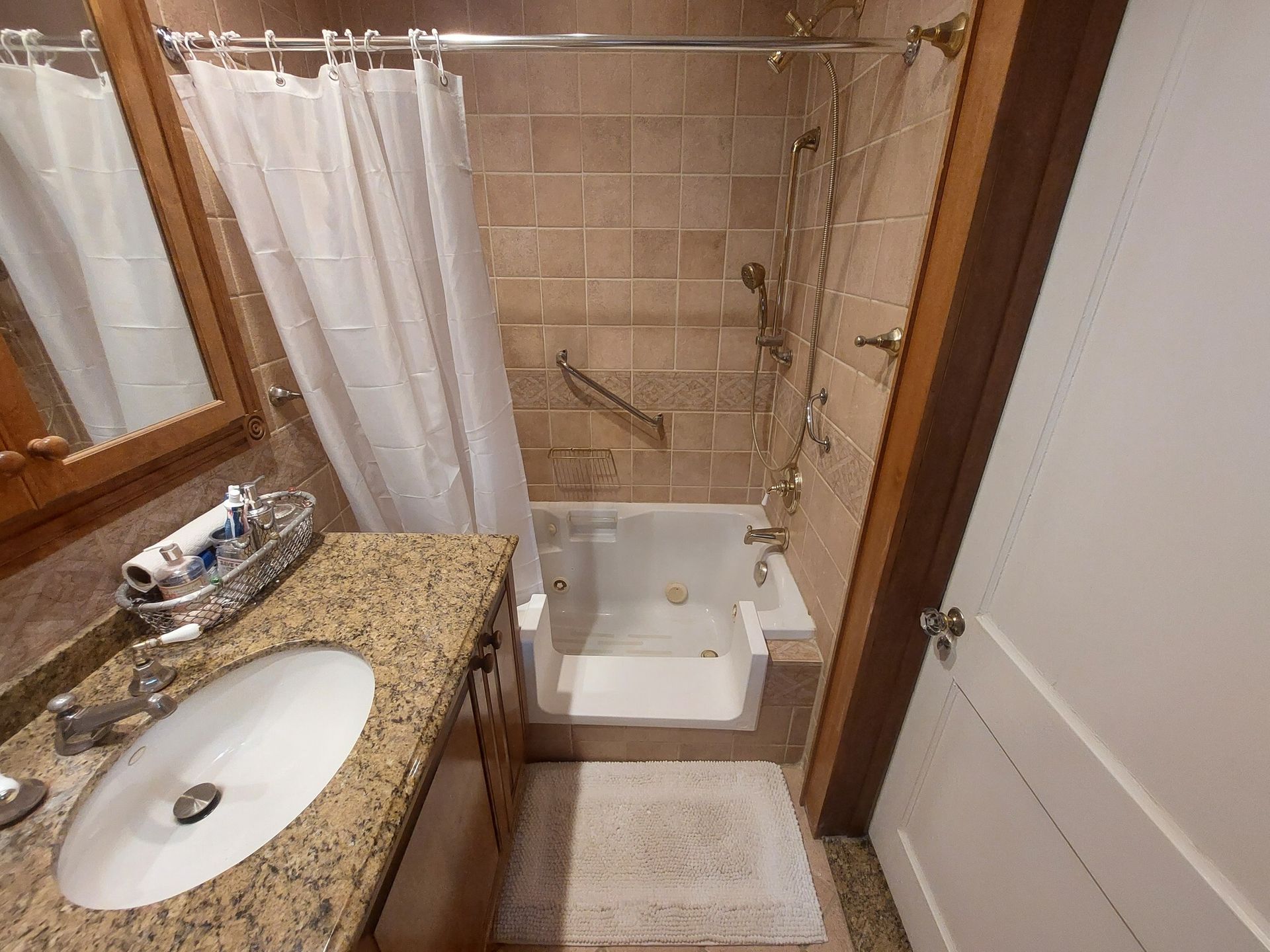 Bathroom with step-in tub and shower, granite vanity sink, mirror, and white door.
