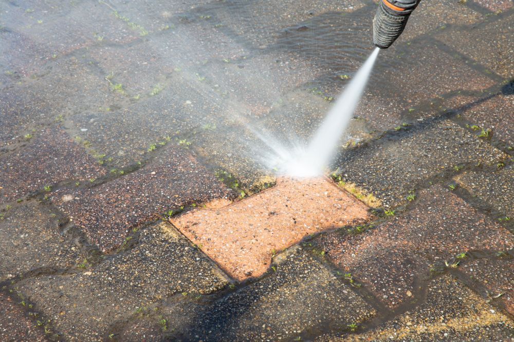 A Person is Using a High Pressure Washer to Clean a Brick Pavement — Doobies Cleaning Service in Port Macquarie, NSW