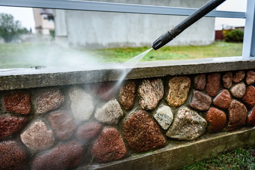A Person is Using a High Pressure Washer to Clean a Stone Wall — Doobies Cleaning Service in Port Macquarie, NSW