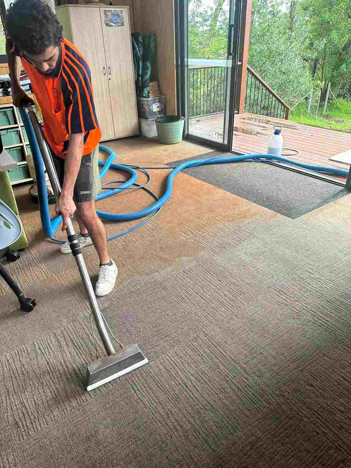 A Man is Using a Vacuum Cleaner to Clean a Carpet in a Room — Doobies Cleaning Service in Port Macquarie, NSW