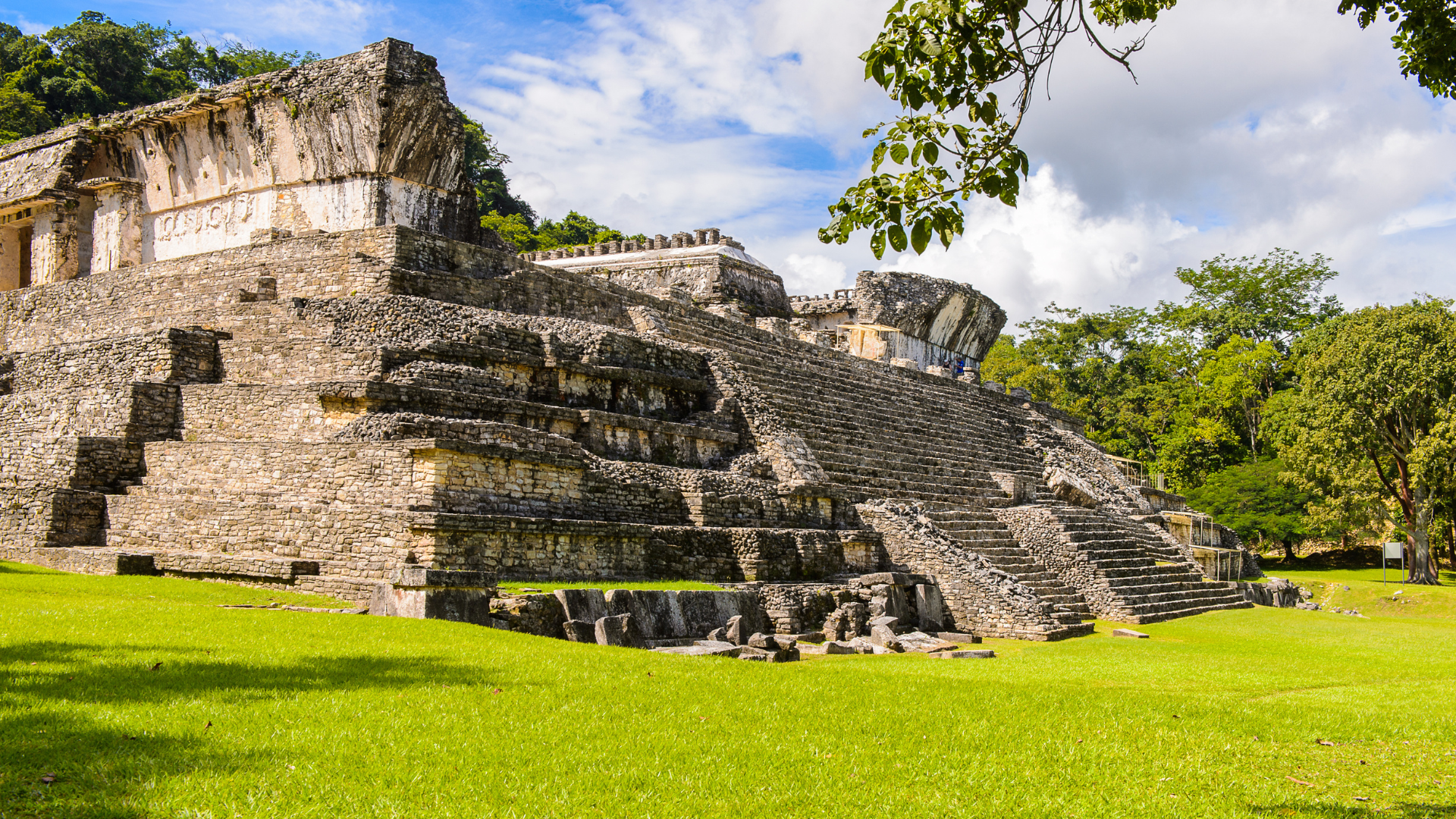 a large stone building temple is sitting in the middle of a grassy field surrounded by trees .
